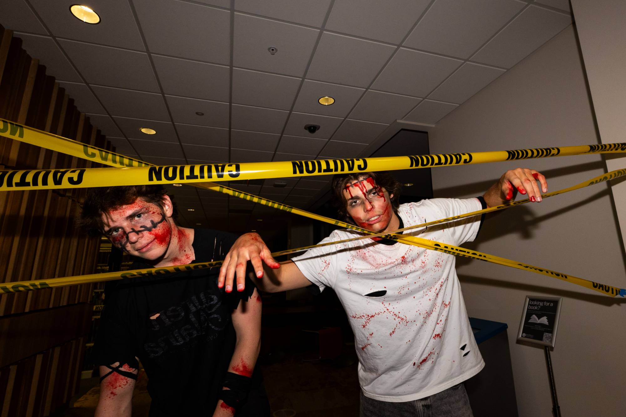 two male students dressed up as zombies posing with caution tape